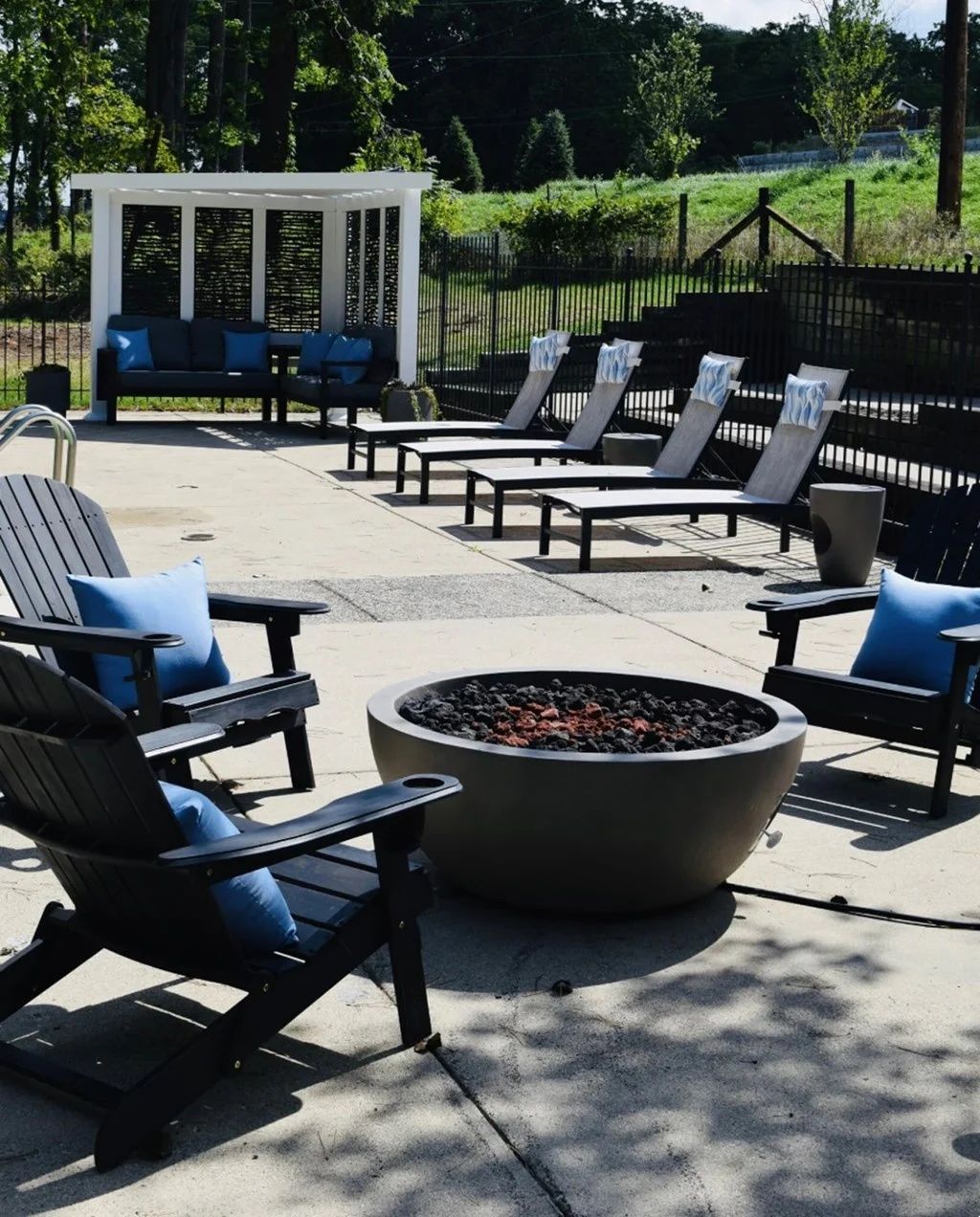 Outdoor patio with black chairs around a round fire pit and a white cabana in the background