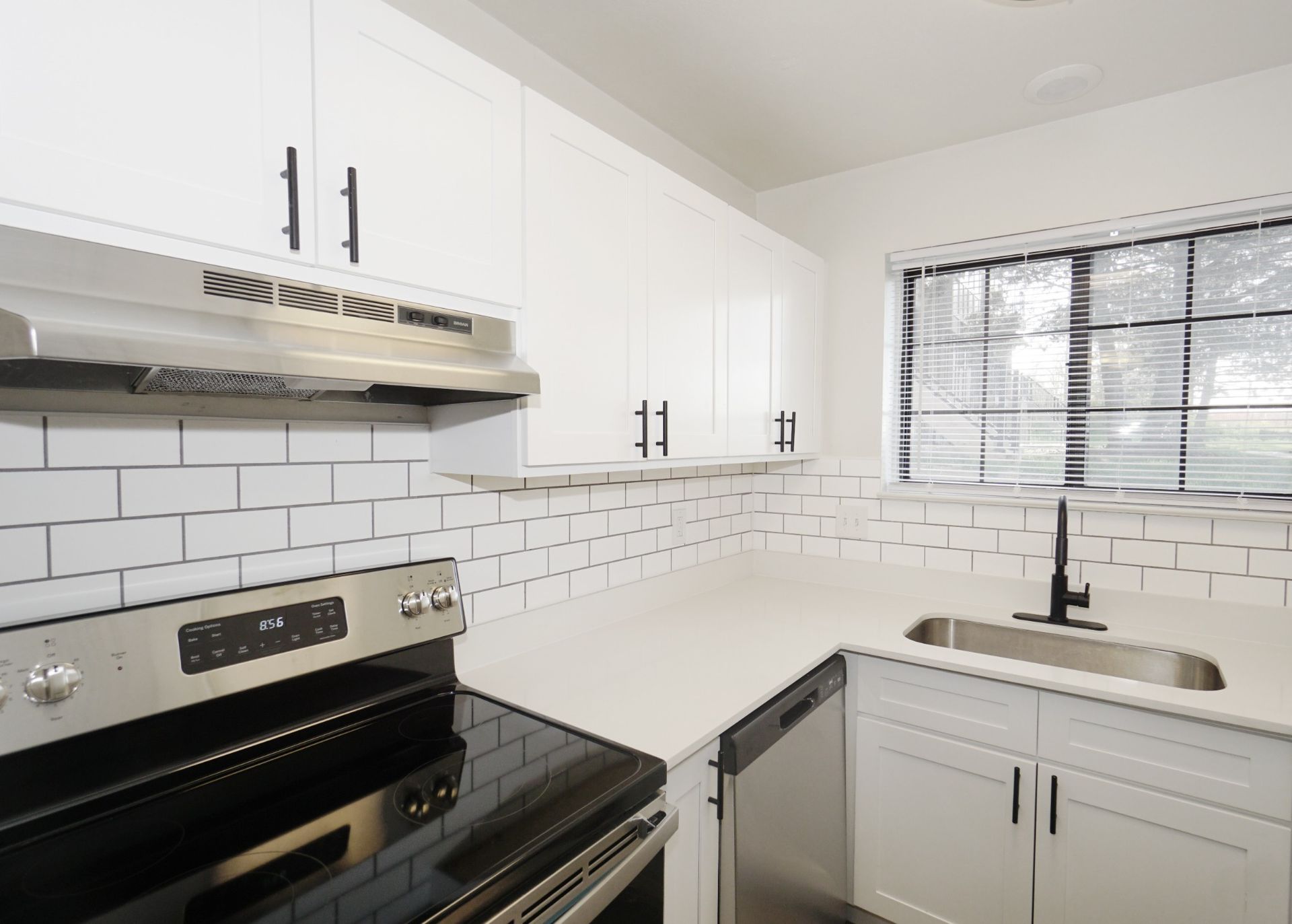 Bright white kitchen with stainless stove, subway tile backsplash, and black faucet by a window