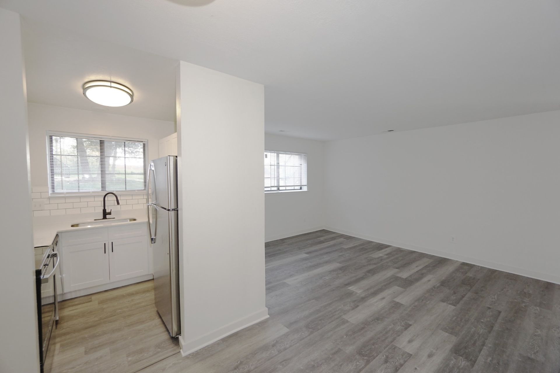Empty open-plan room with gray floors, white walls, and a small kitchen area by a window.