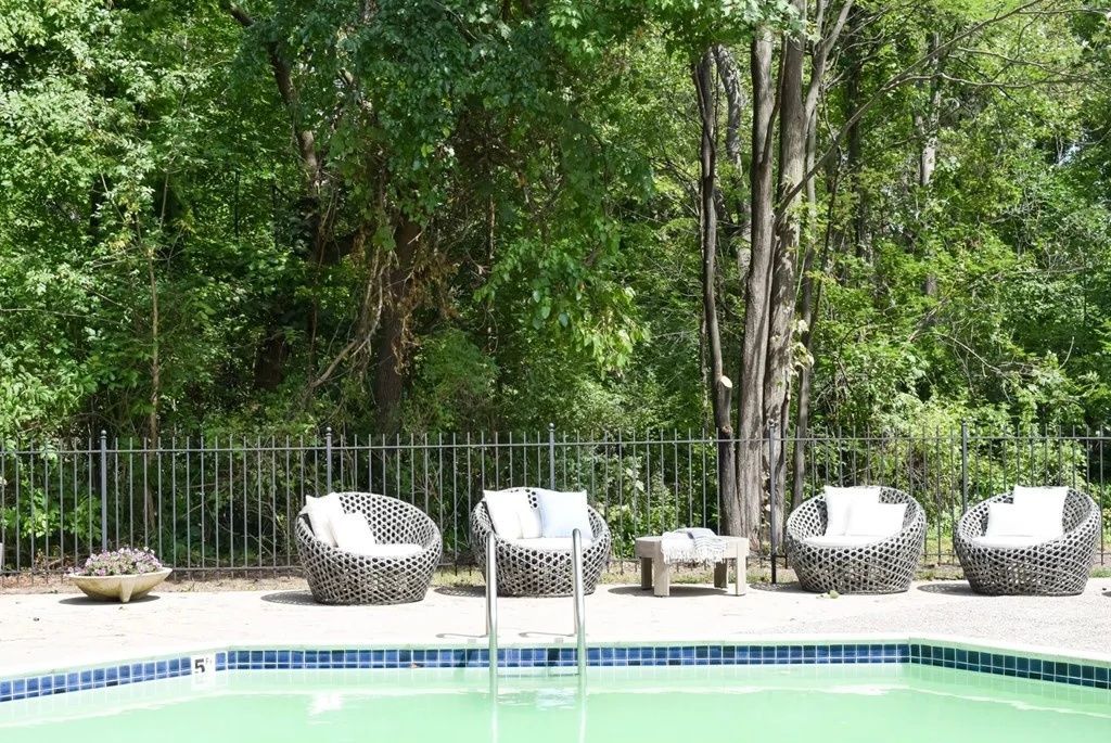 Poolside lounge chairs beside a turquoise pool, with trees and greenery in the background.