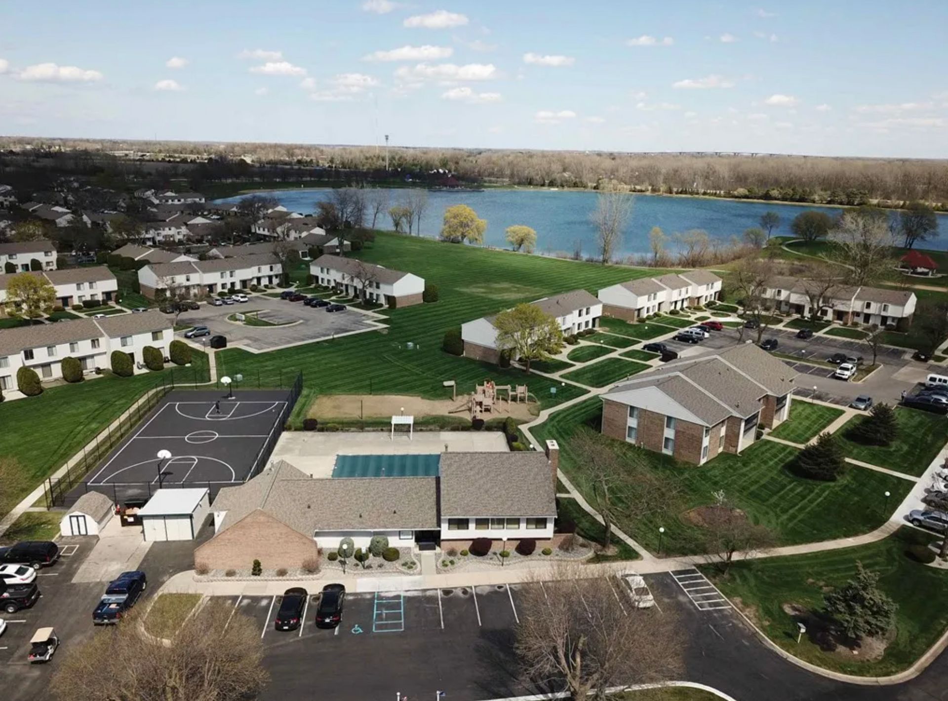 Aerial view of a lakeside residential complex with apartments, parking lots, and a basketball court