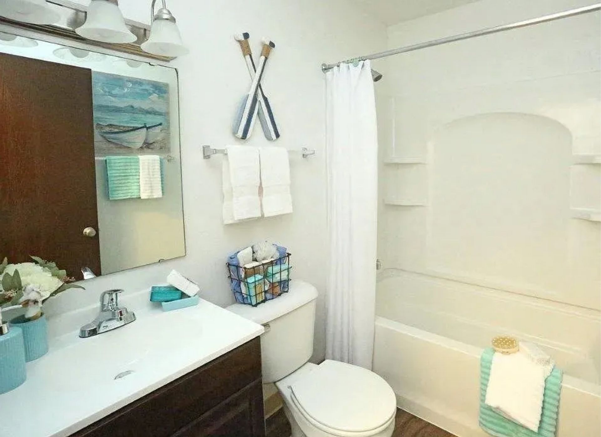 Small bathroom with white tub, sink, toilet, mirror, and teal accents