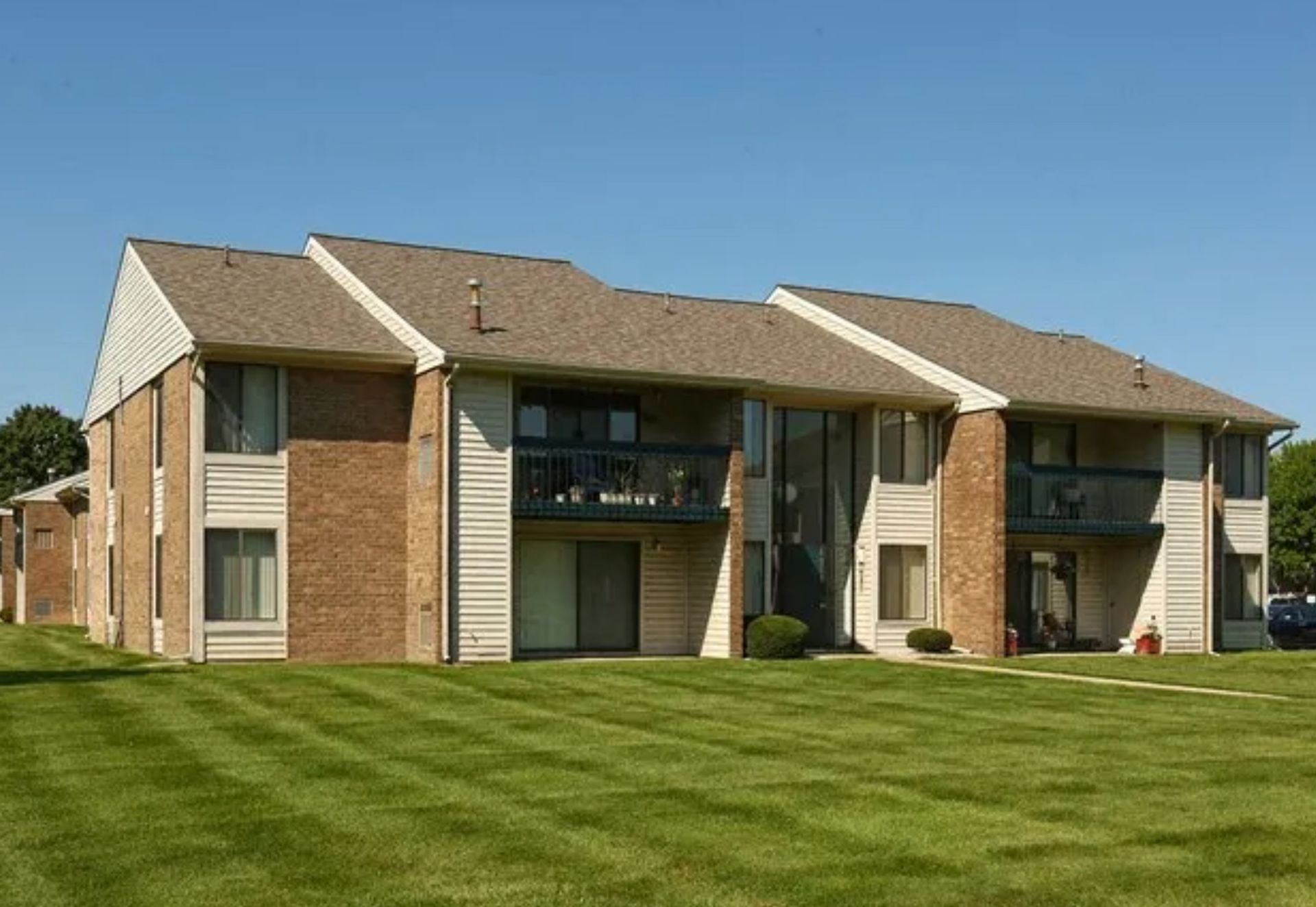 Two-story brick apartment building with balconies and a large green lawn under a blue sky