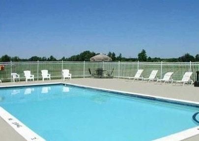 Outdoor swimming pool with blue water, white lounge chairs, and a fence under a clear sky