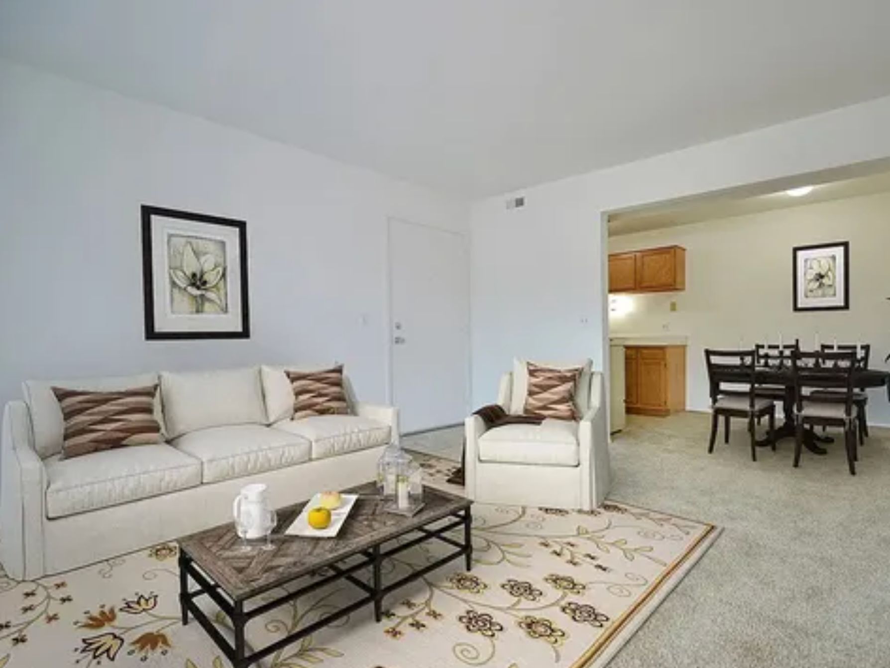 Bright living room with white sofa, armchair, glass coffee table, and dining area beyond