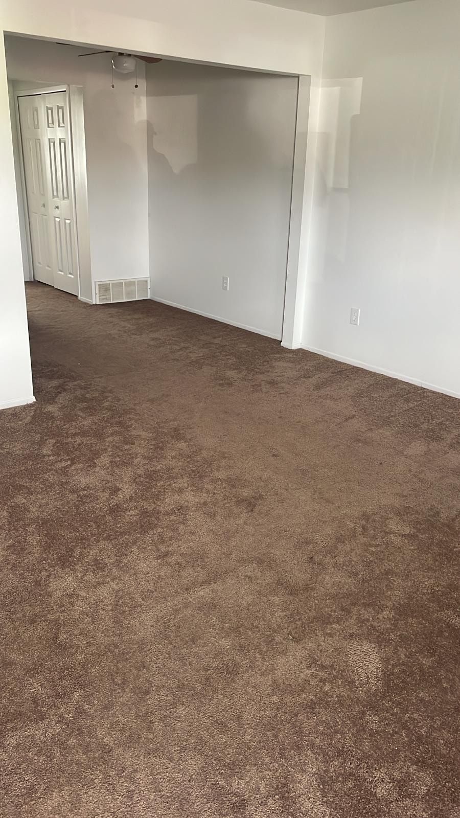 Empty carpeted room with white walls, open doorway, and a closet visible in the back.