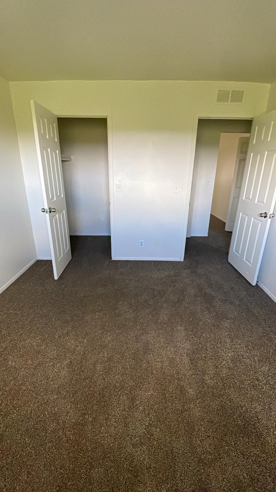 Empty beige bedroom with open double doors and brown carpet