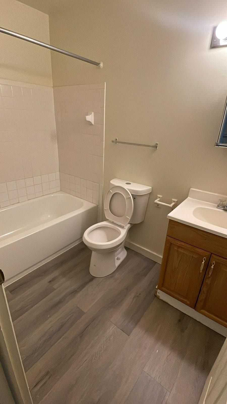 Small bathroom with tub, toilet, sink, and gray wood-look flooring.