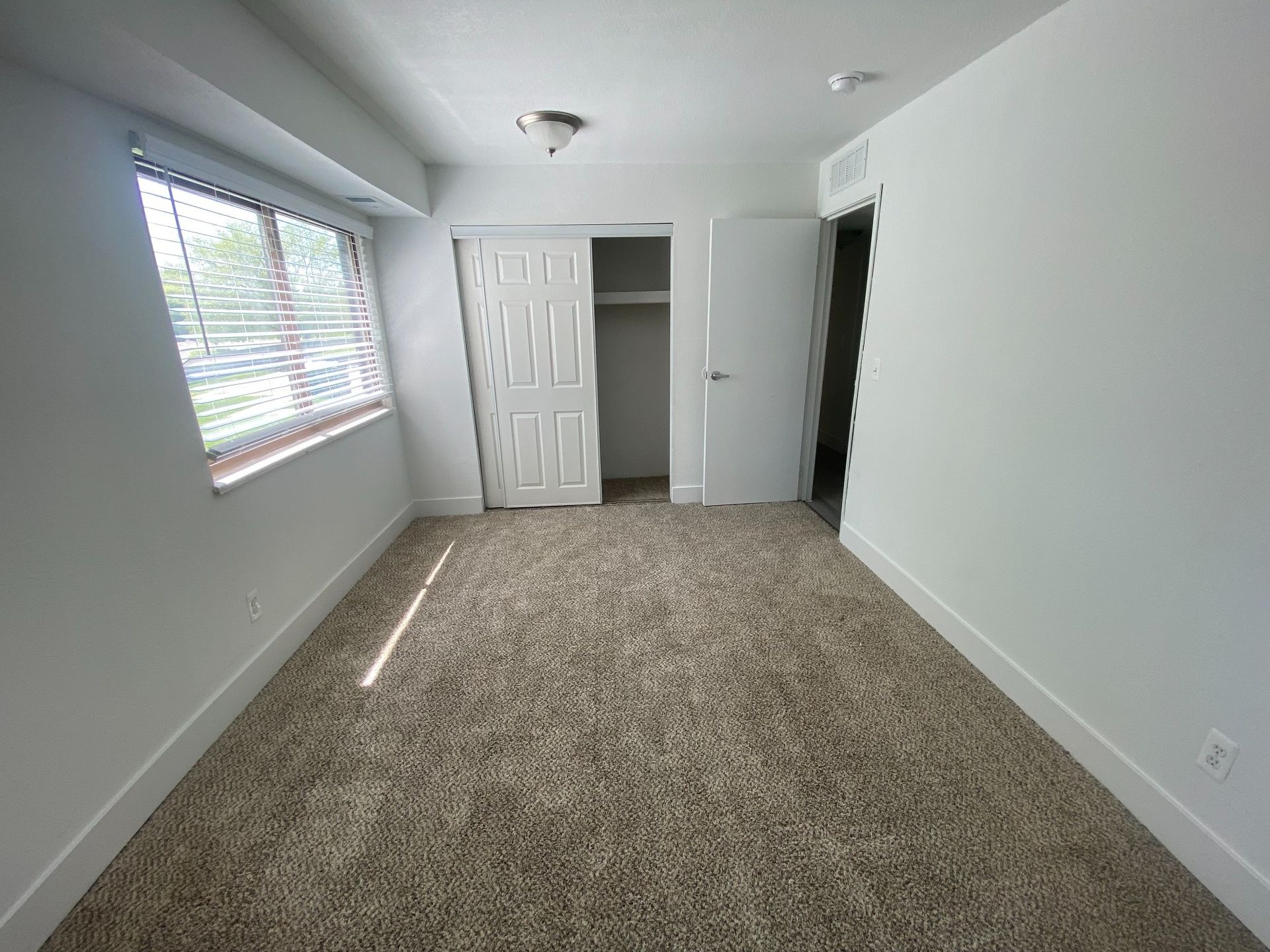 Empty gray bedroom with carpet, window blinds, ceiling fan, and open closet doors