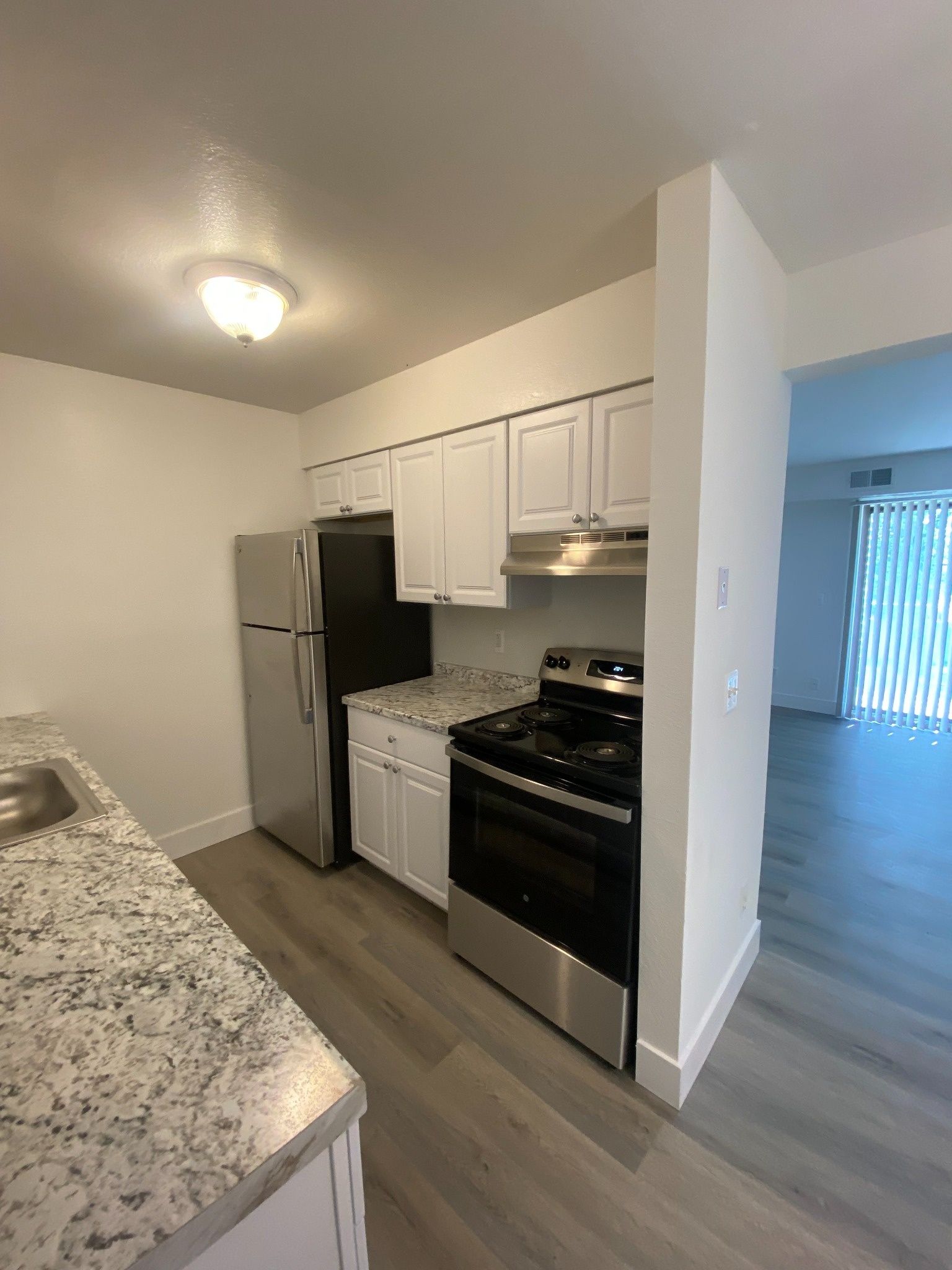 Small kitchen with white cabinets, stainless steel appliances, and granite countertops opening to a living area