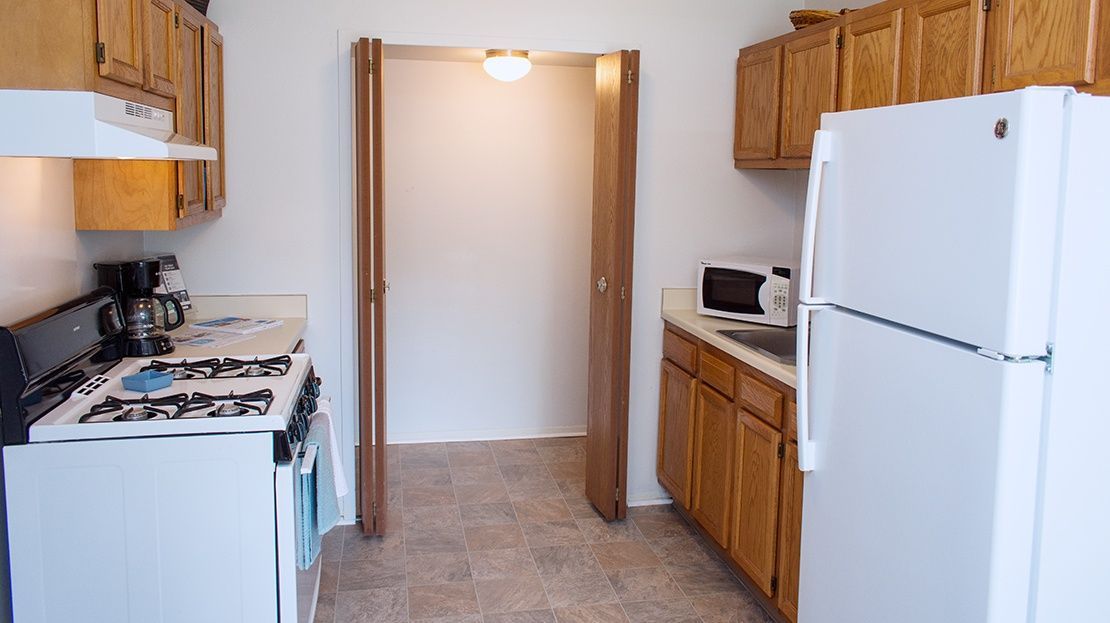 Small kitchen with white appliances, wood cabinets, and a doorway to another room.