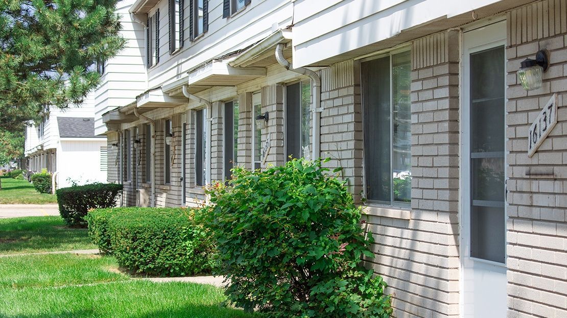 Apartment building exterior with white brick walls, windows, and green shrubs along a grassy walkway