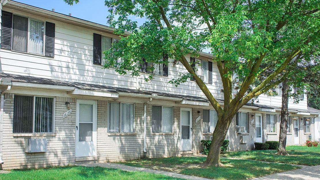 Two-story apartment building with white siding and a large tree in front