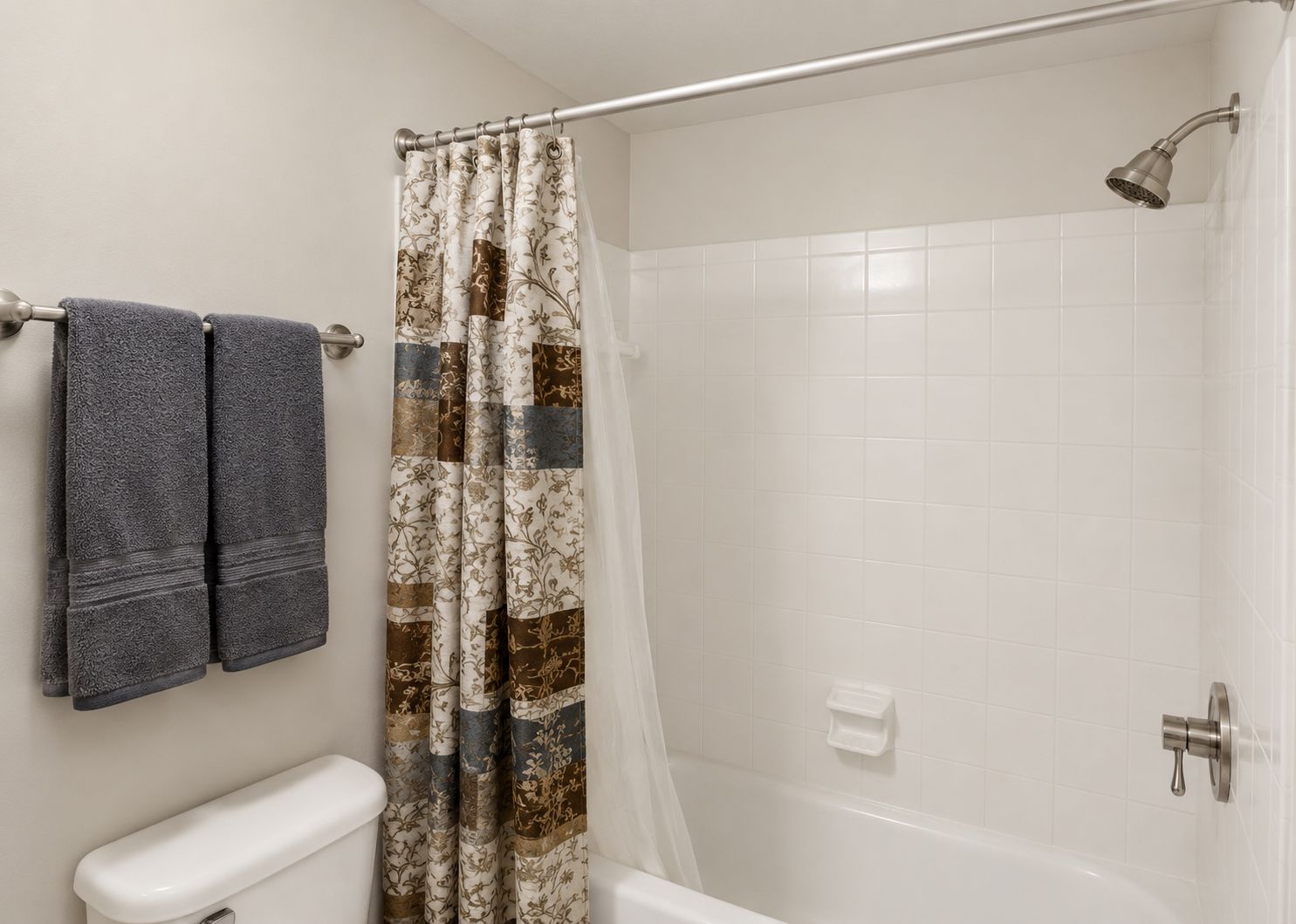 Bathroom with tub, shower curtain, towel rack, and gray towels on a beige wall.