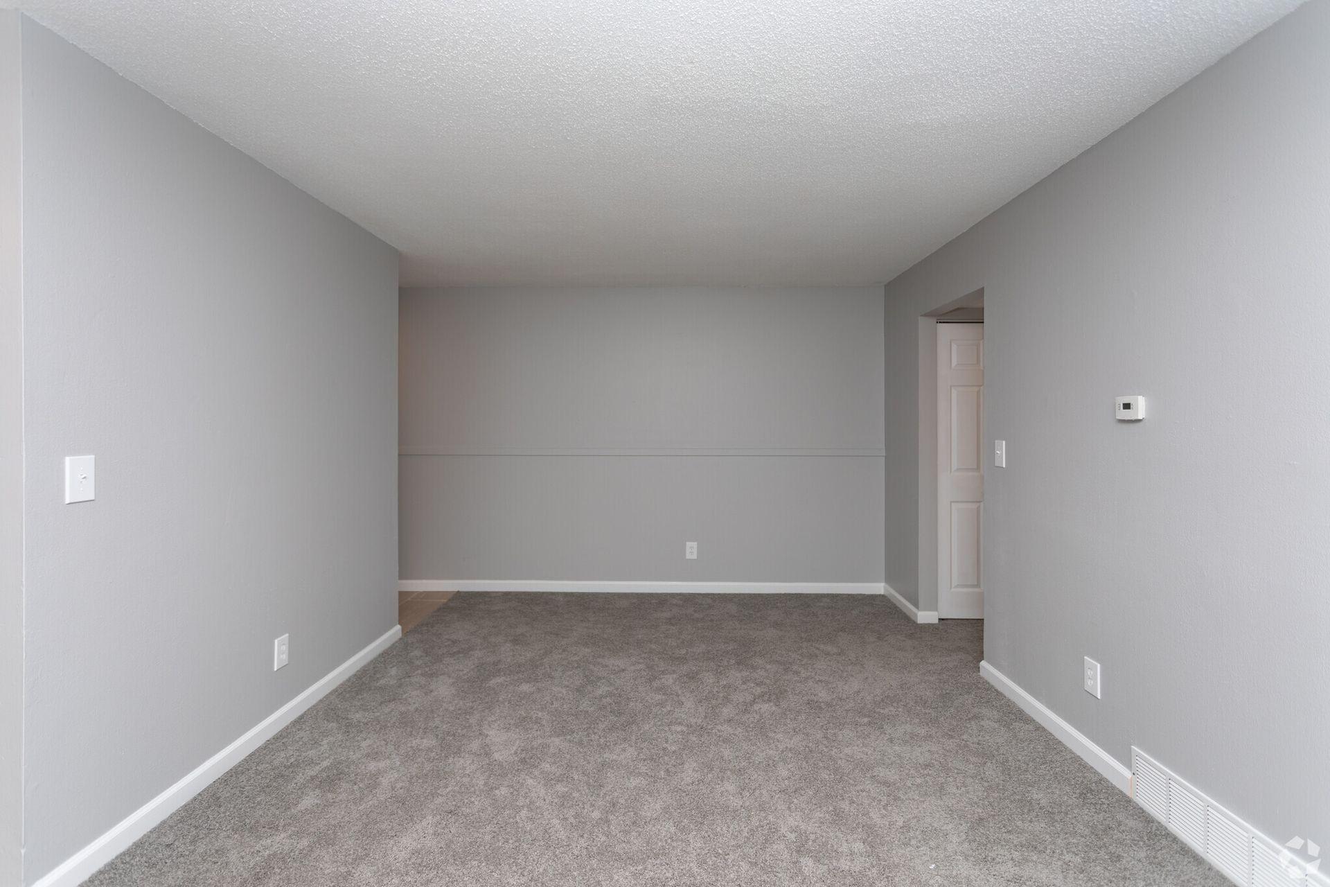 Empty gray carpeted living room with recessed wall and doorway on the right.
