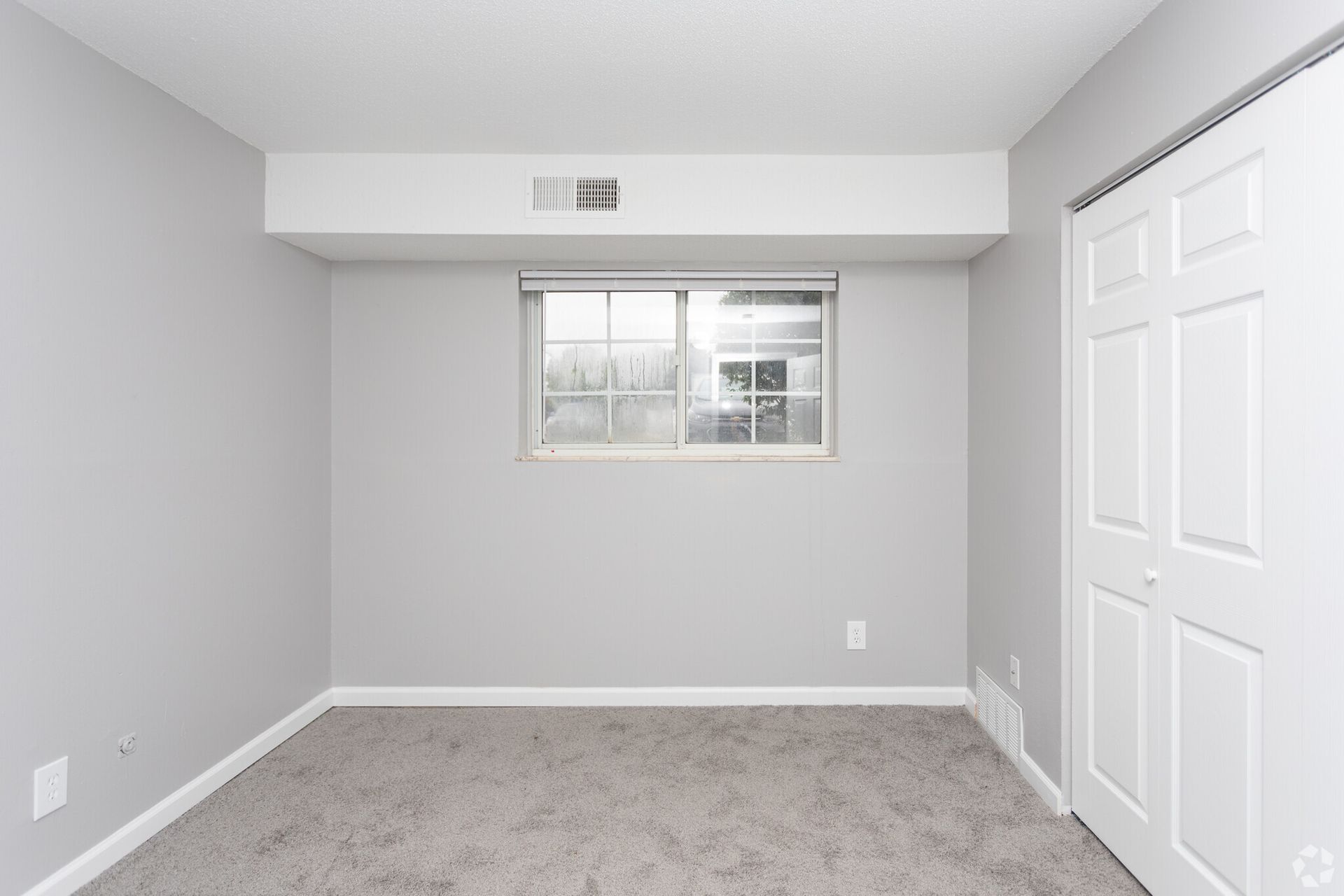 Empty gray bedroom with carpet, window, and white closet doors