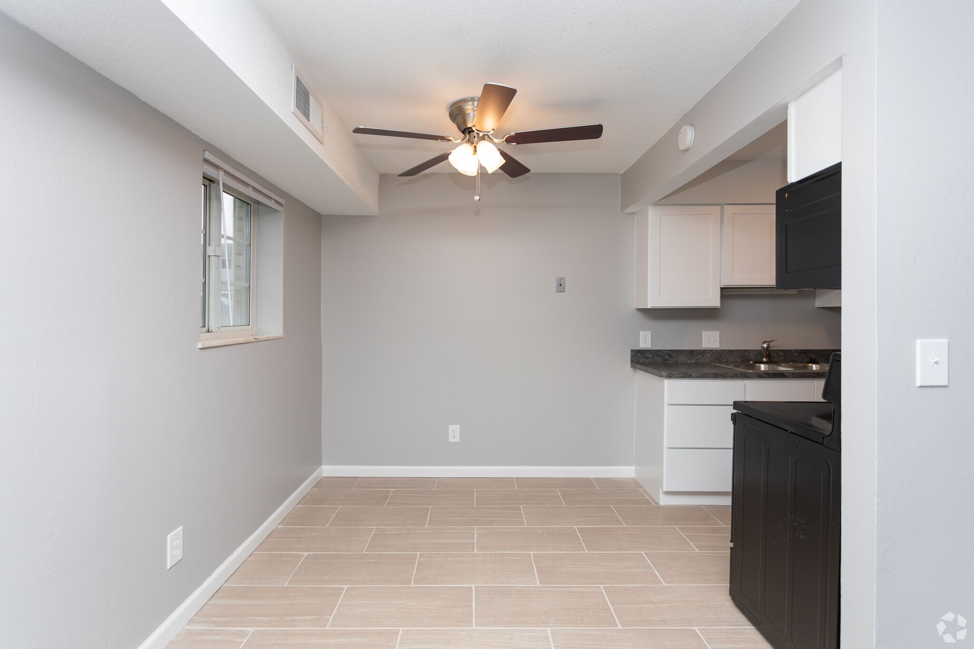 Empty modern kitchen and dining area with gray walls, tile floor, and ceiling fan