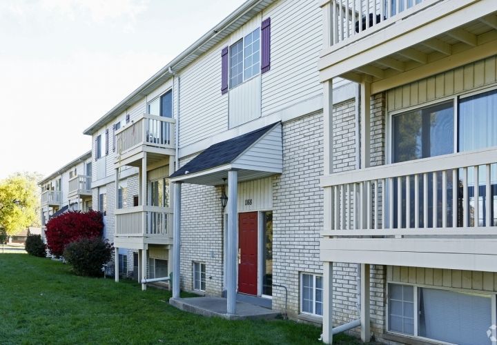 Apartment building exterior with white balconies, red door, and green lawn in daylight
