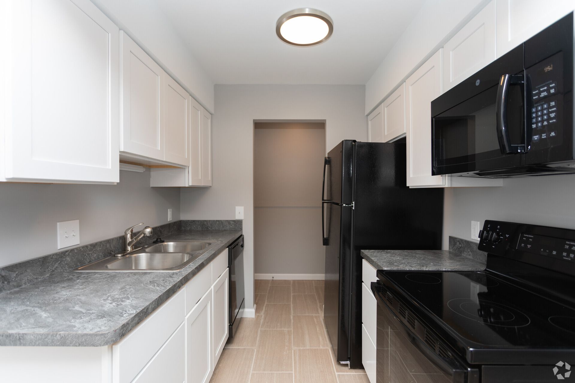 Narrow white kitchen with black appliances, gray countertops, and beige tile flooring