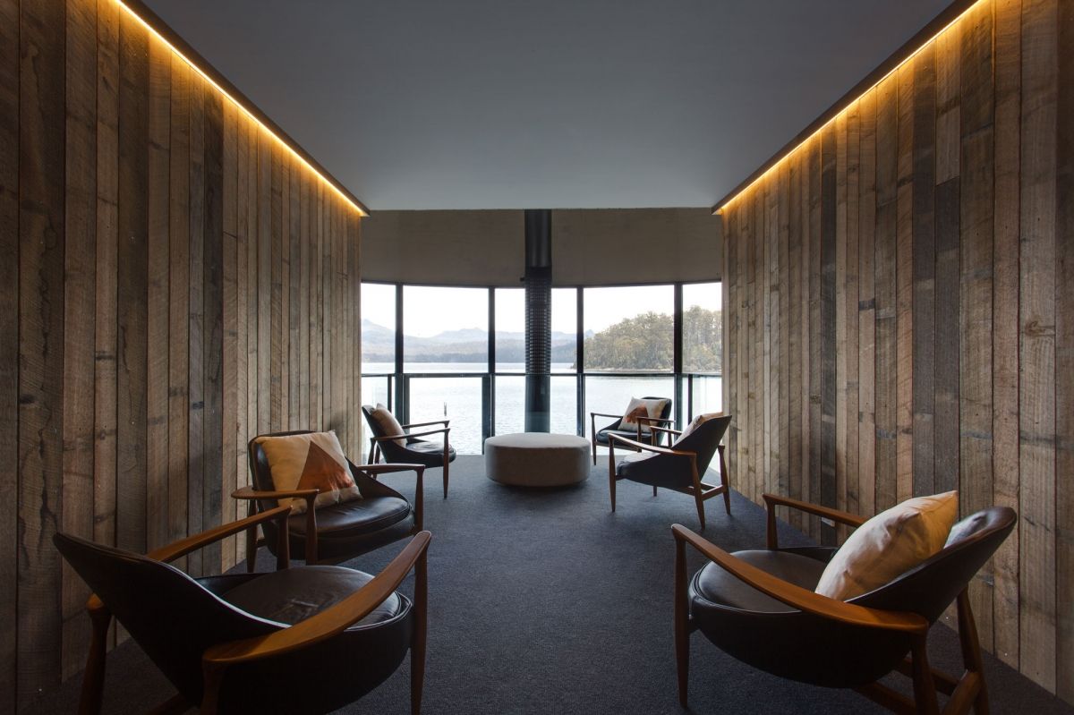 Modern lounge with wood walls, warm lighting, and chairs facing a lake view through large windows