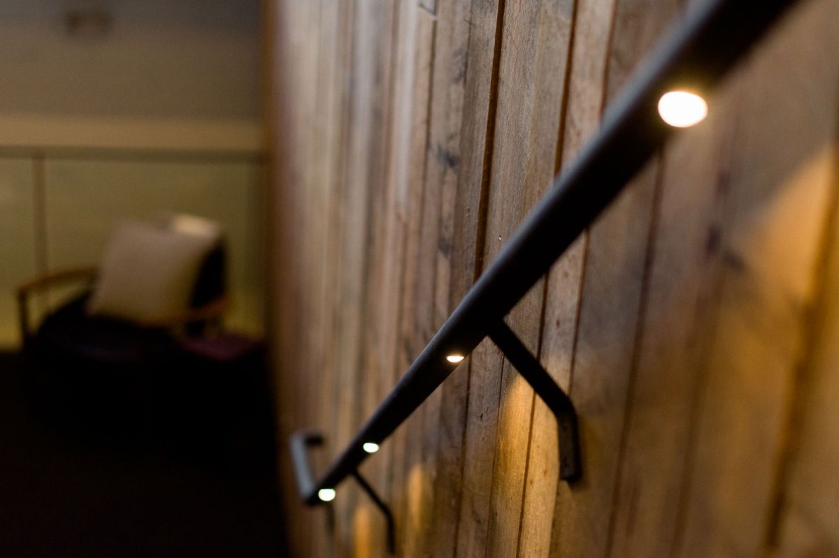 Black handrail with small lights along a wooden staircase wall in a dim hallway