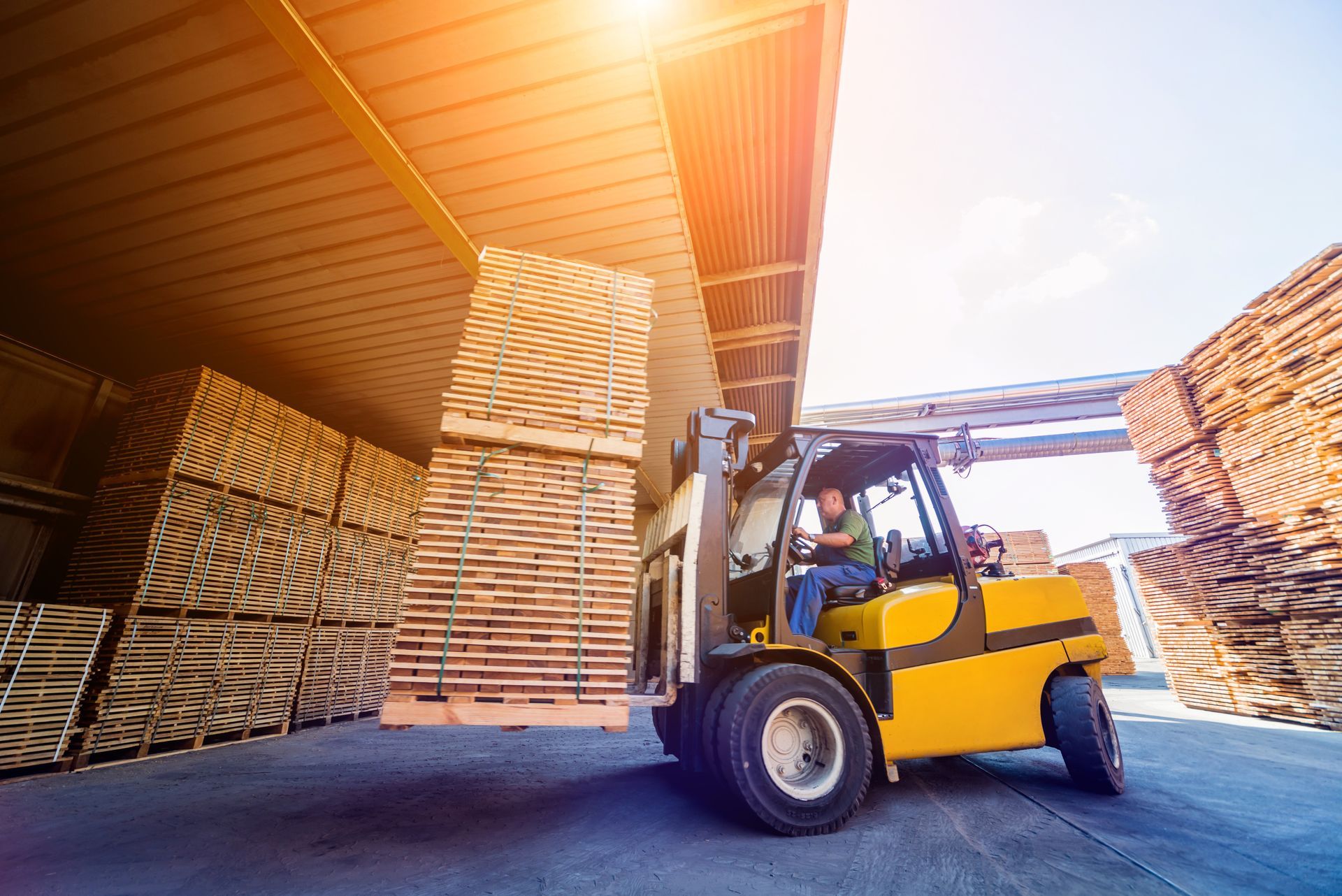 Forklift moving stacked lumber in a warehouse yard at sunset
