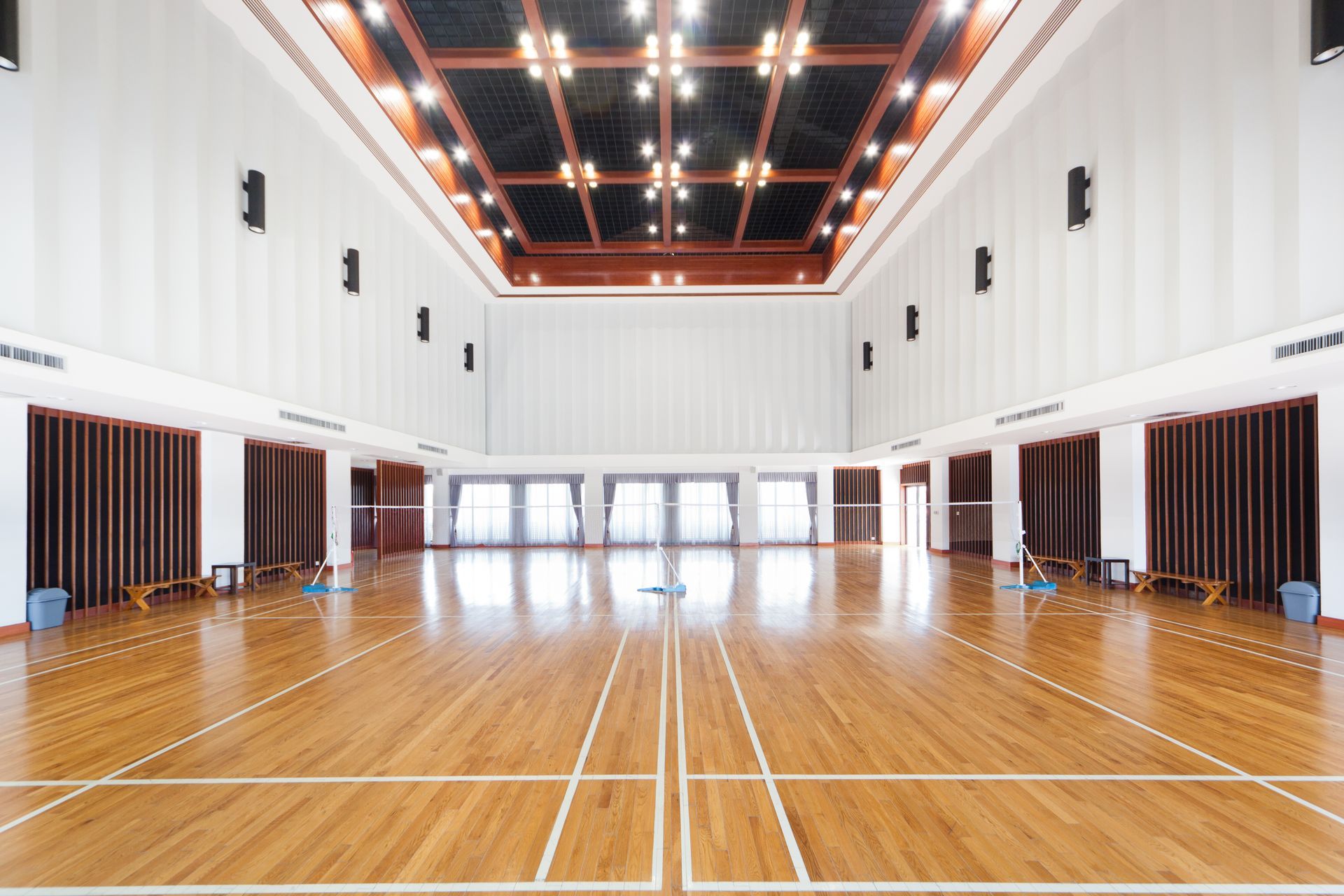 Empty indoor gymnasium with polished wood floor, high white walls, and a dark ceiling with lights