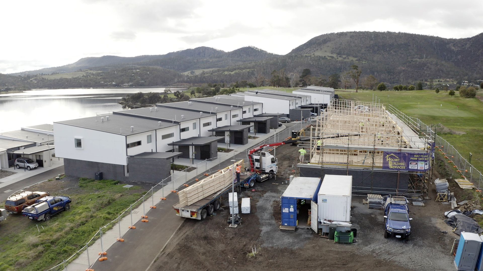 Aerial view of a large industrial site with white buildings, trucks, and equipment near hills and water.