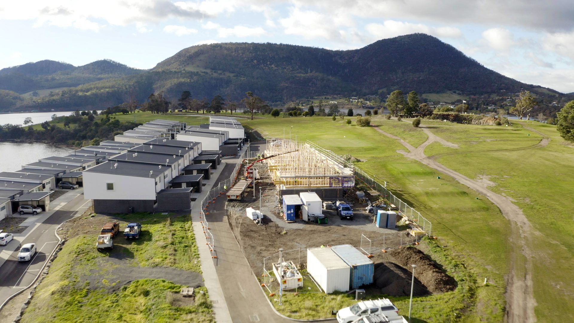 Aerial view of industrial buildings and trailers beside a grassy field, with hills in the background.