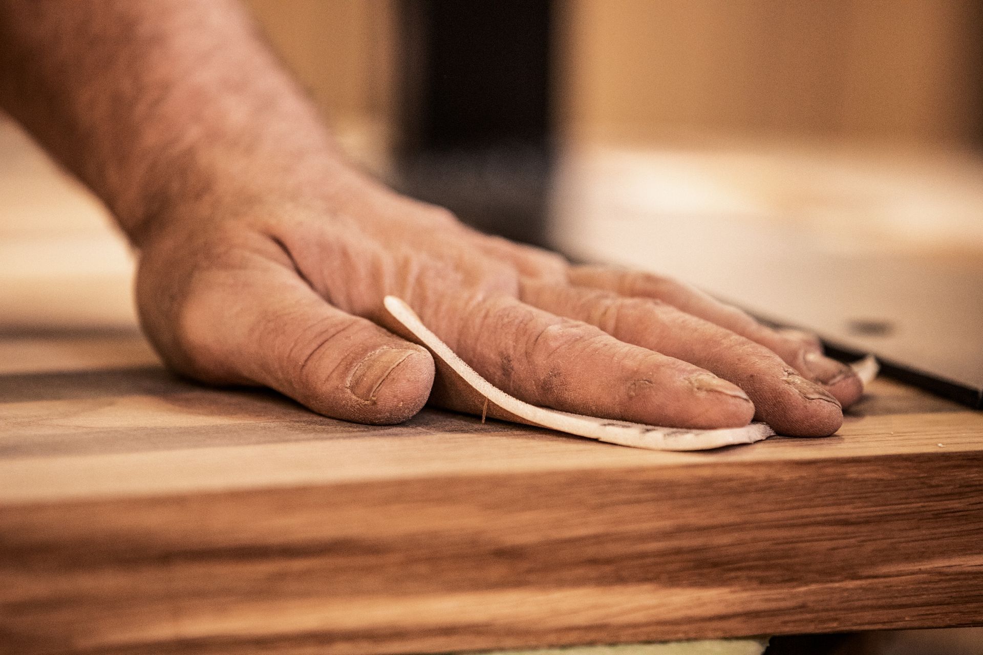 A mature carpenter smoothing a Tasmanian Oak plank with sandpaper during custom joinery work.
