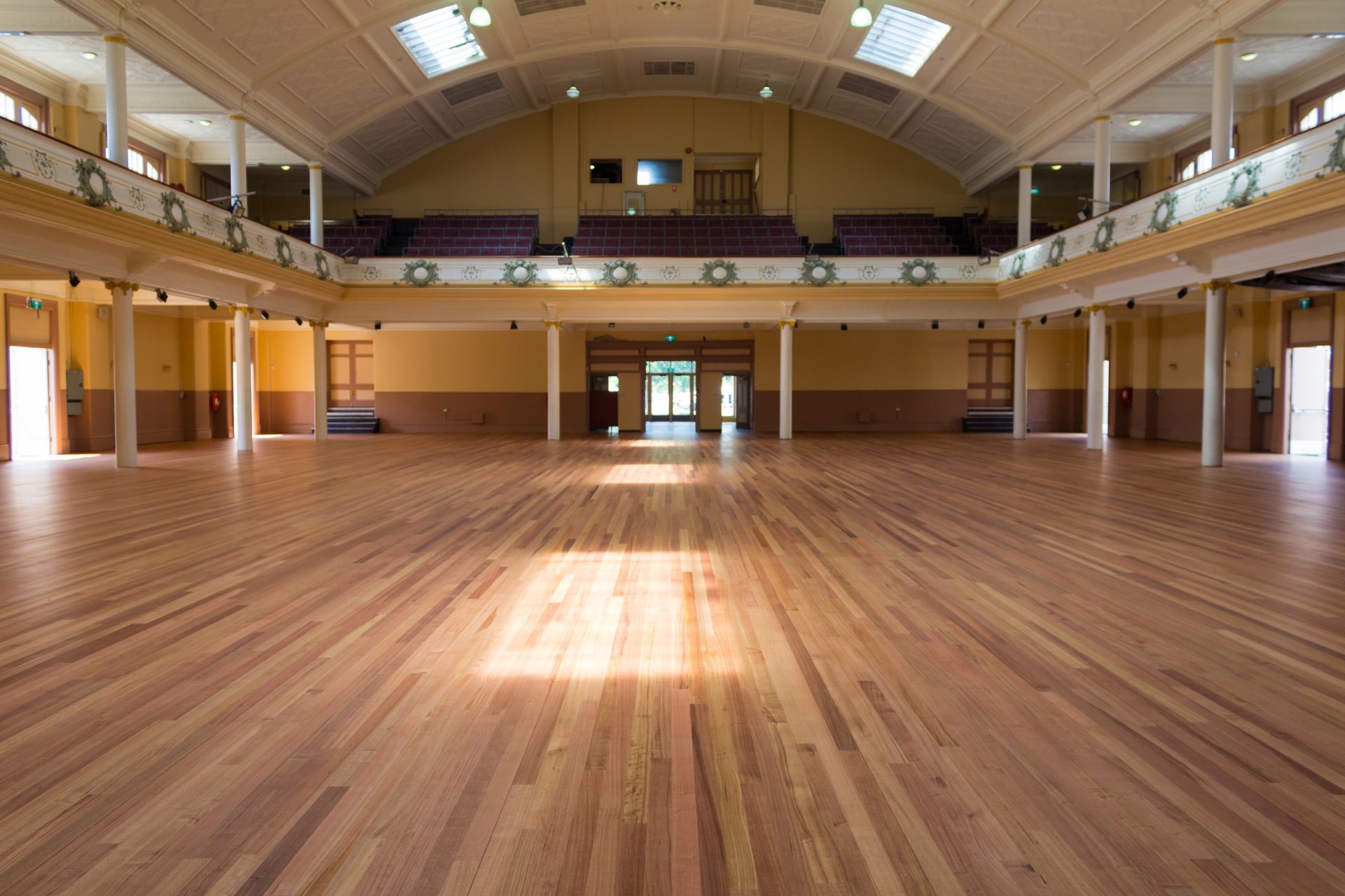 Empty wooden gymnasium with polished floor and high arched ceiling, lit by skylights