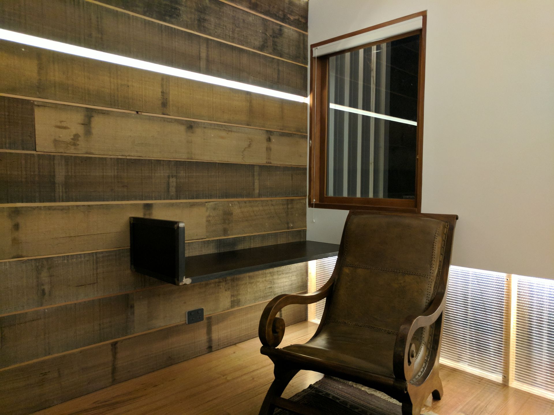 Modern room with a brown armchair, wall-mounted shelf, and wood-paneled walls by a window.