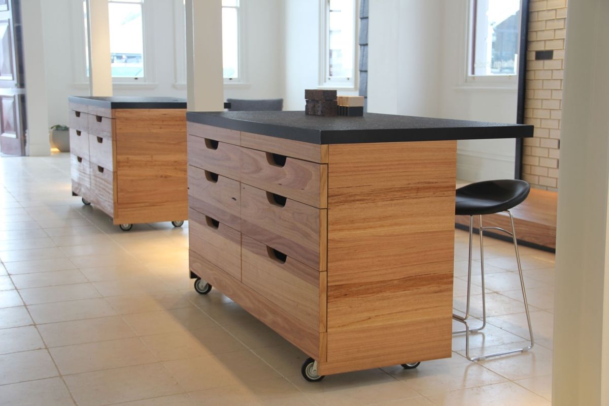 Modern kitchen islands with black countertops and wooden drawers on casters in a bright room