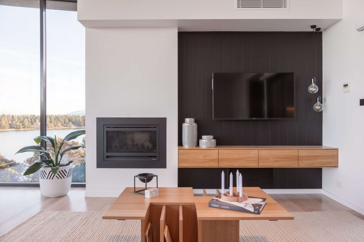 Modern living room with wall-mounted TV, fireplace, wood console, and large window view