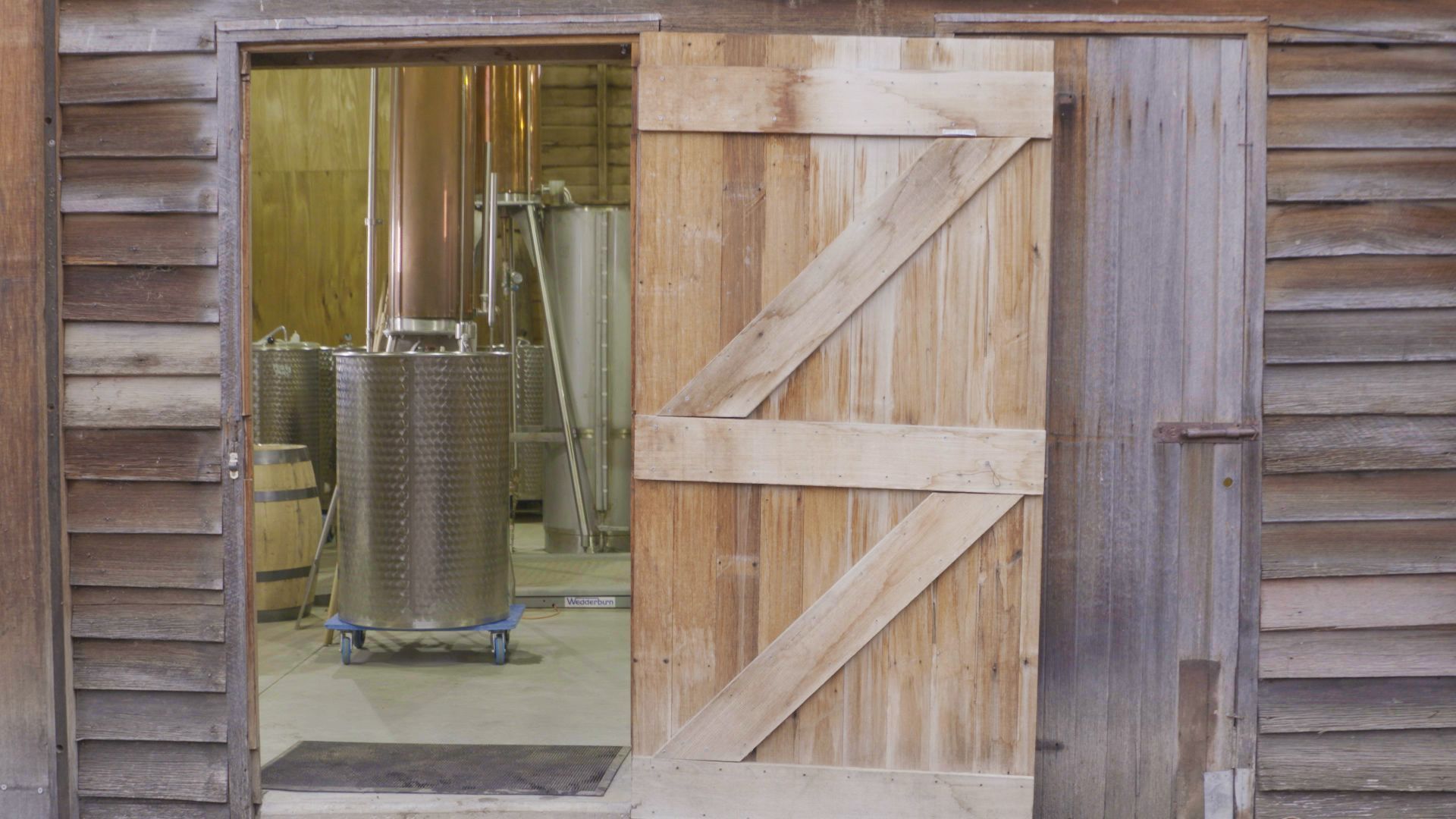 Open wooden barn door revealing a metal machine inside a rustic workshop.