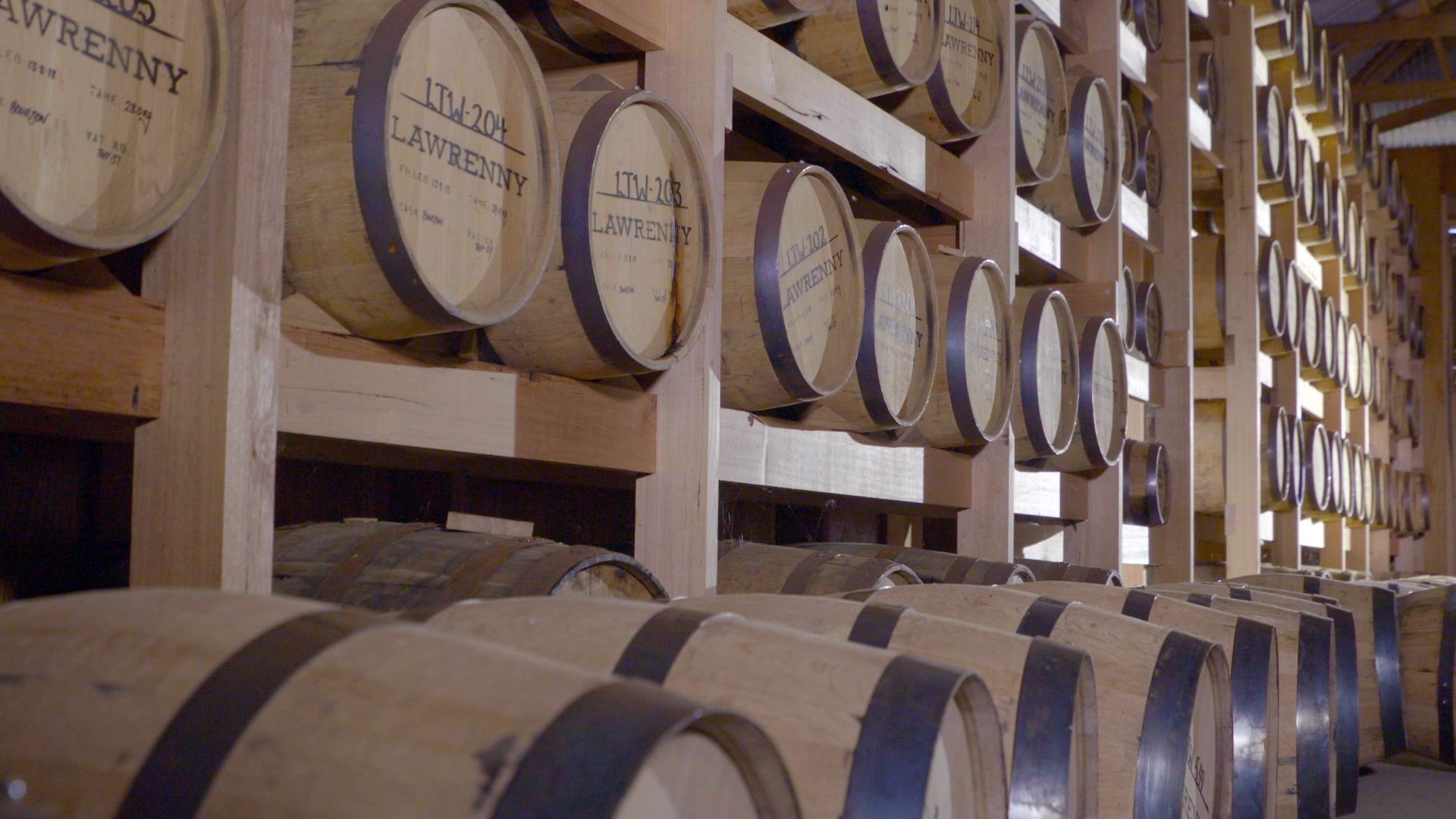 Rows of wooden barrels stacked in a cellar, likely for aging wine or whiskey.