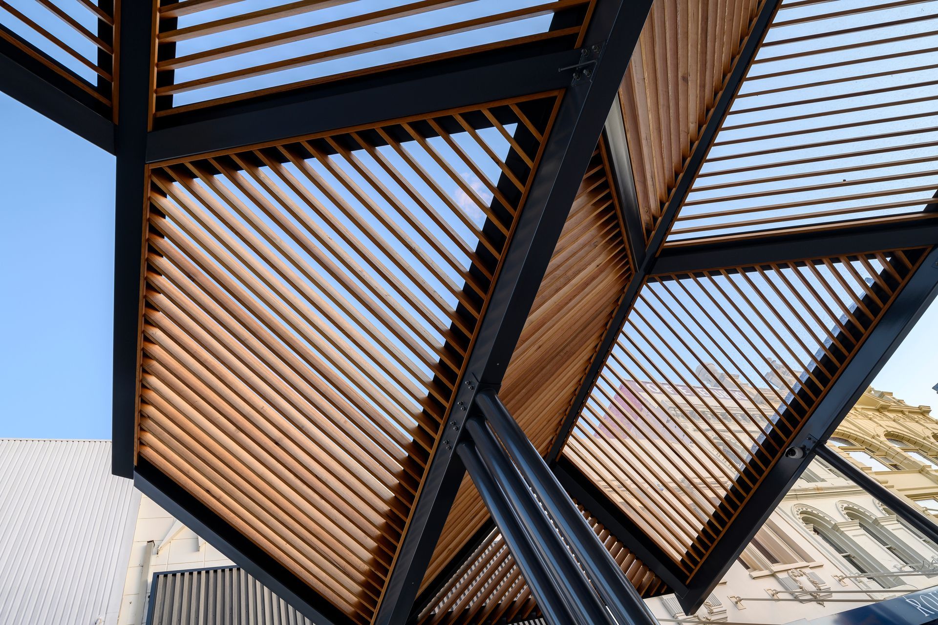 Modern metal pergola with slatted wooden panels casting striped shadows against a blue sky