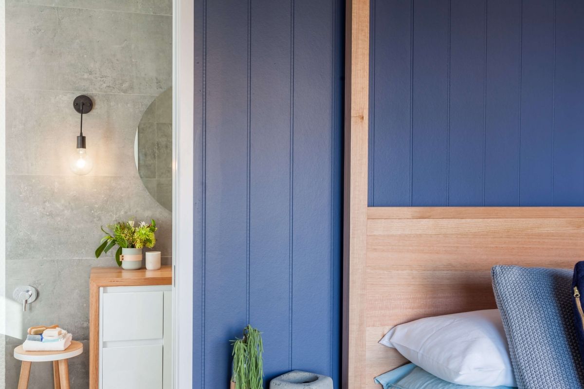 Blue-and-wood bedroom with a bed, mirrored wall, small dresser, and wall sconce lighting