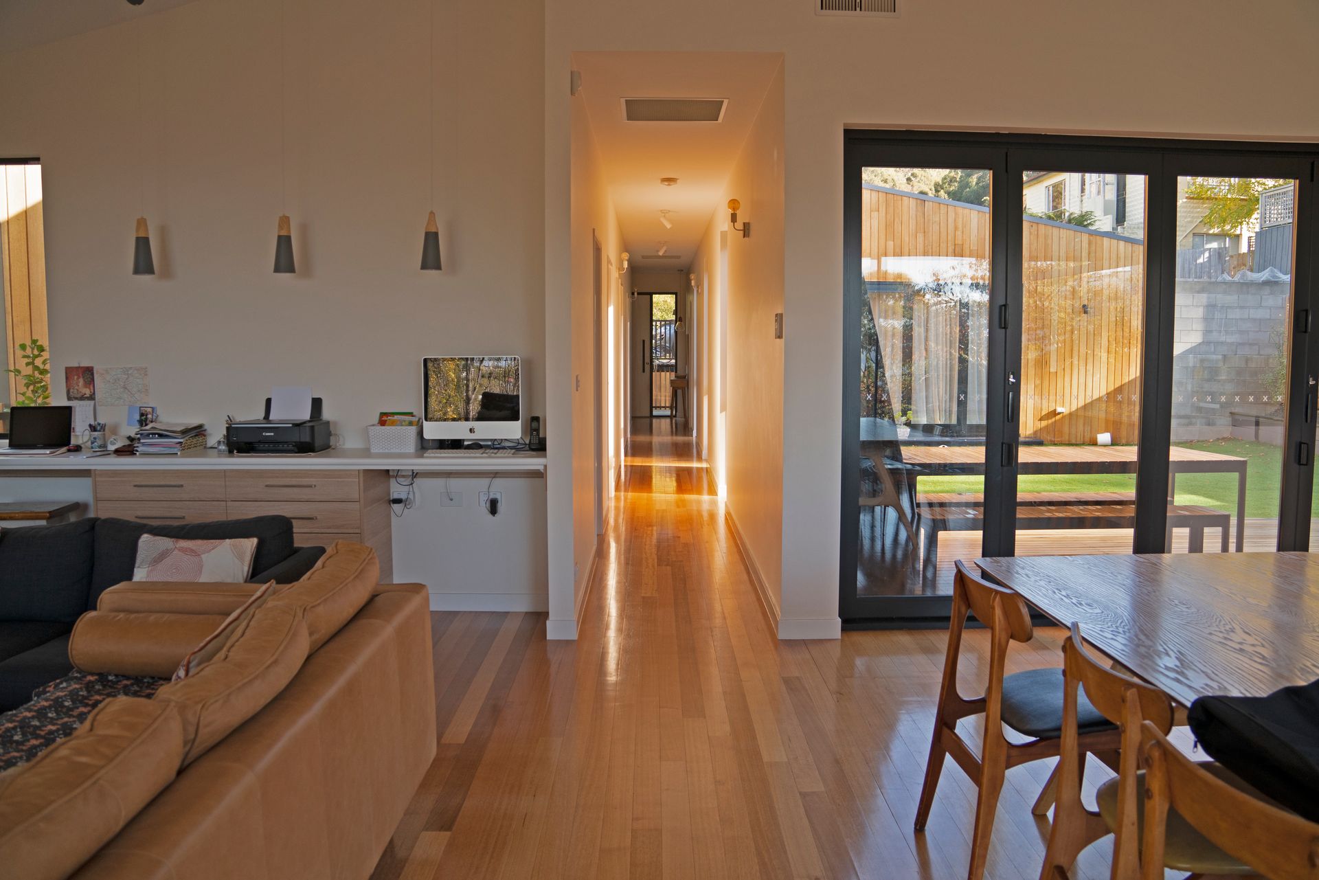 Open-plan living room with sofa, dining table, and hallway leading to a bright sliding glass door