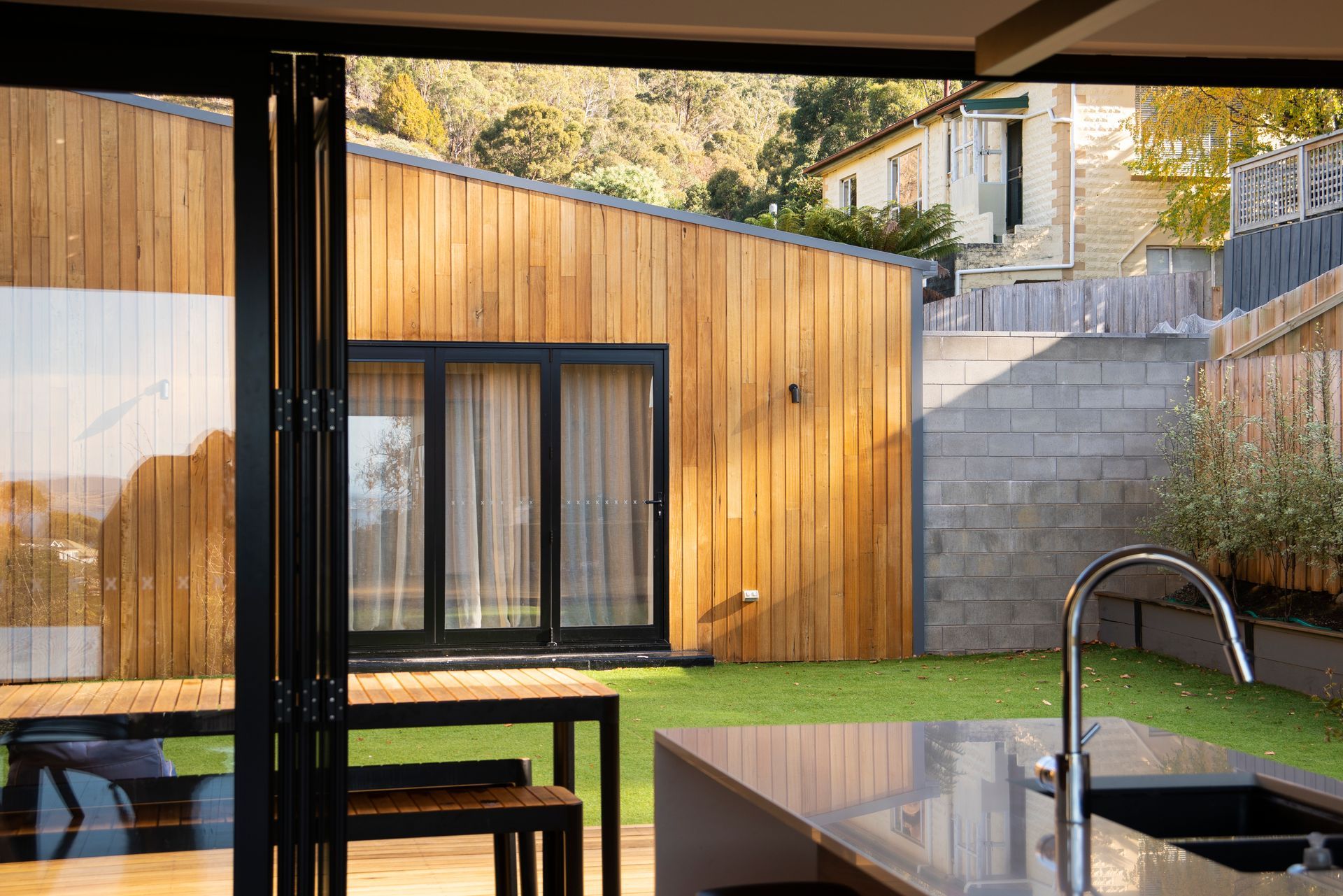 Modern patio with wood-paneled walls, sliding doors, grass courtyard, and stone steps beside a kitchen sink
