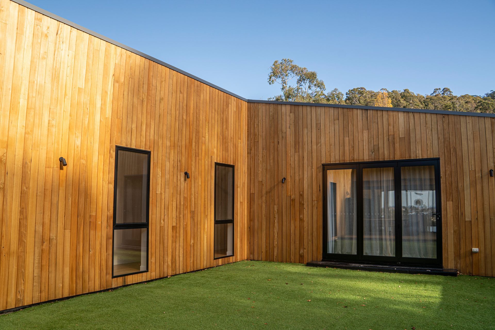 Modern wooden building with tall windows and glass doors beside a green lawn