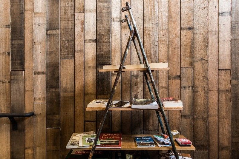 A wooden shelving unit with books against a rustic wood plank wall.
