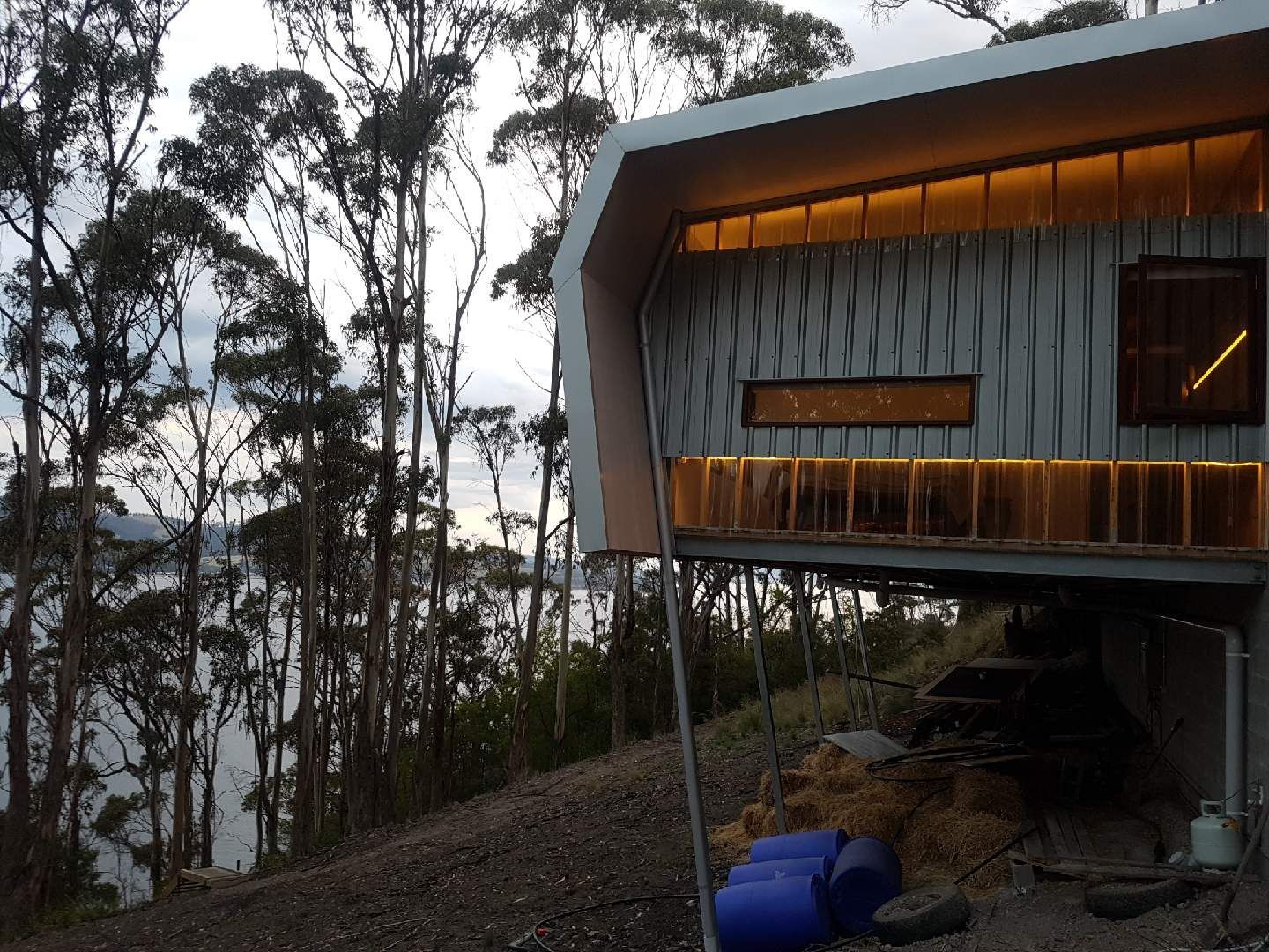 Modern cabin cantilevered over a forested hillside at dusk, with warm interior lights and large windows.