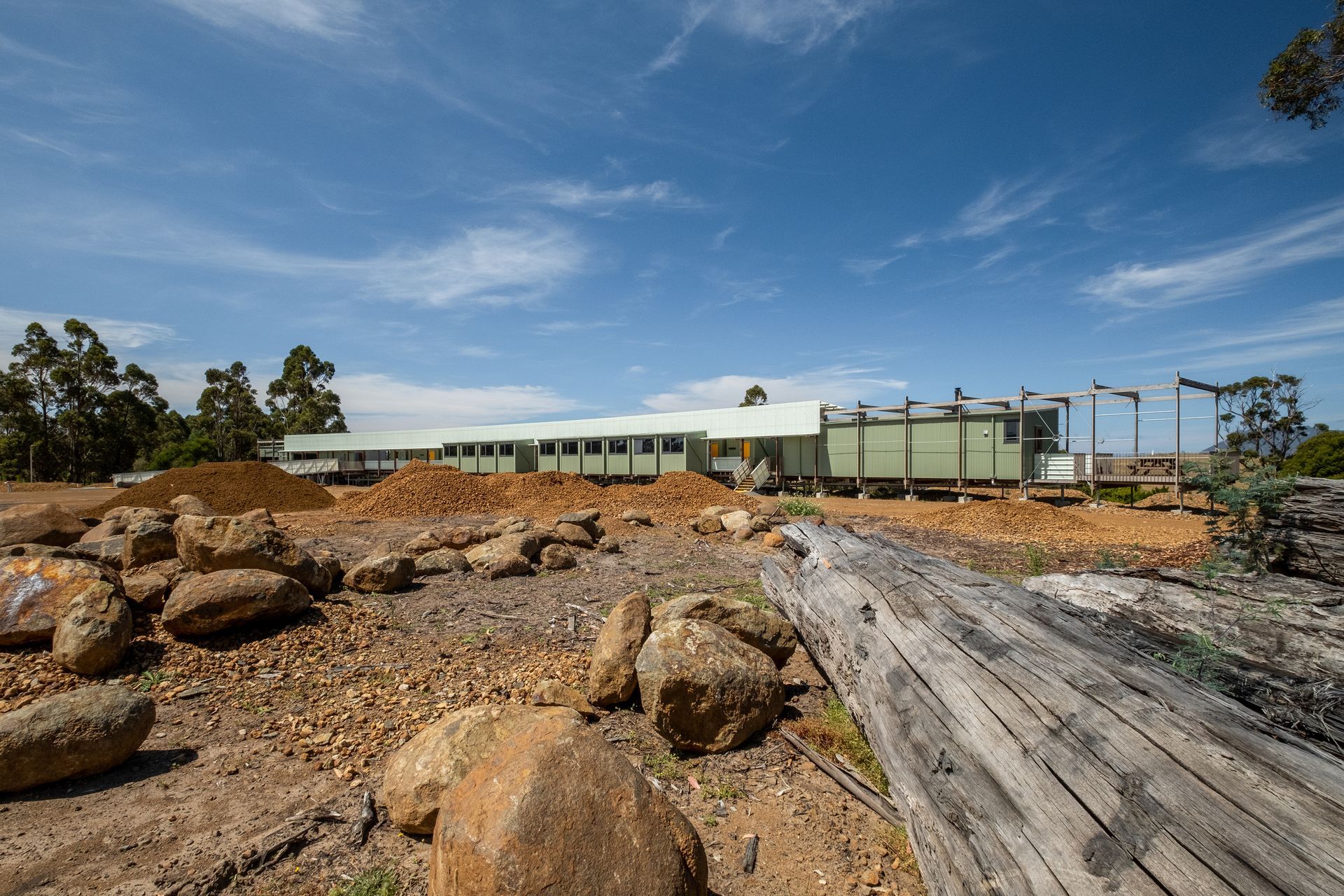 Rural building under blue sky with rocks and driftwood in the foreground