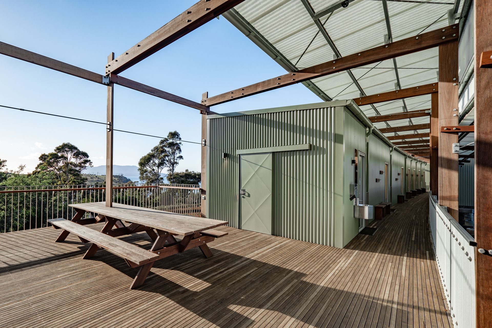 Outdoor wooden deck with picnic table beside a corrugated metal building under a roofed structure