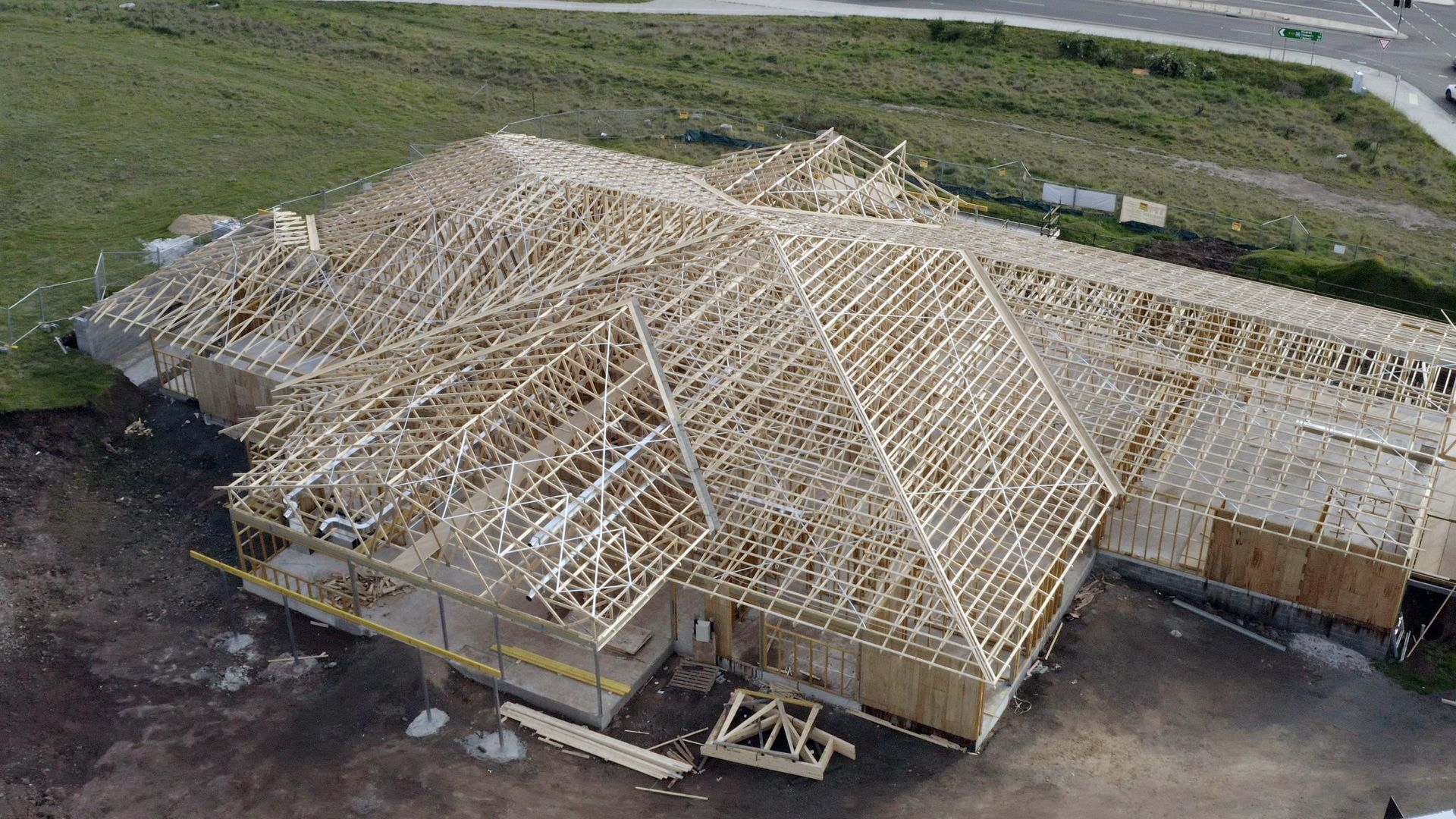 Aerial view of a house under construction with exposed wooden roof framing on a cleared lot.