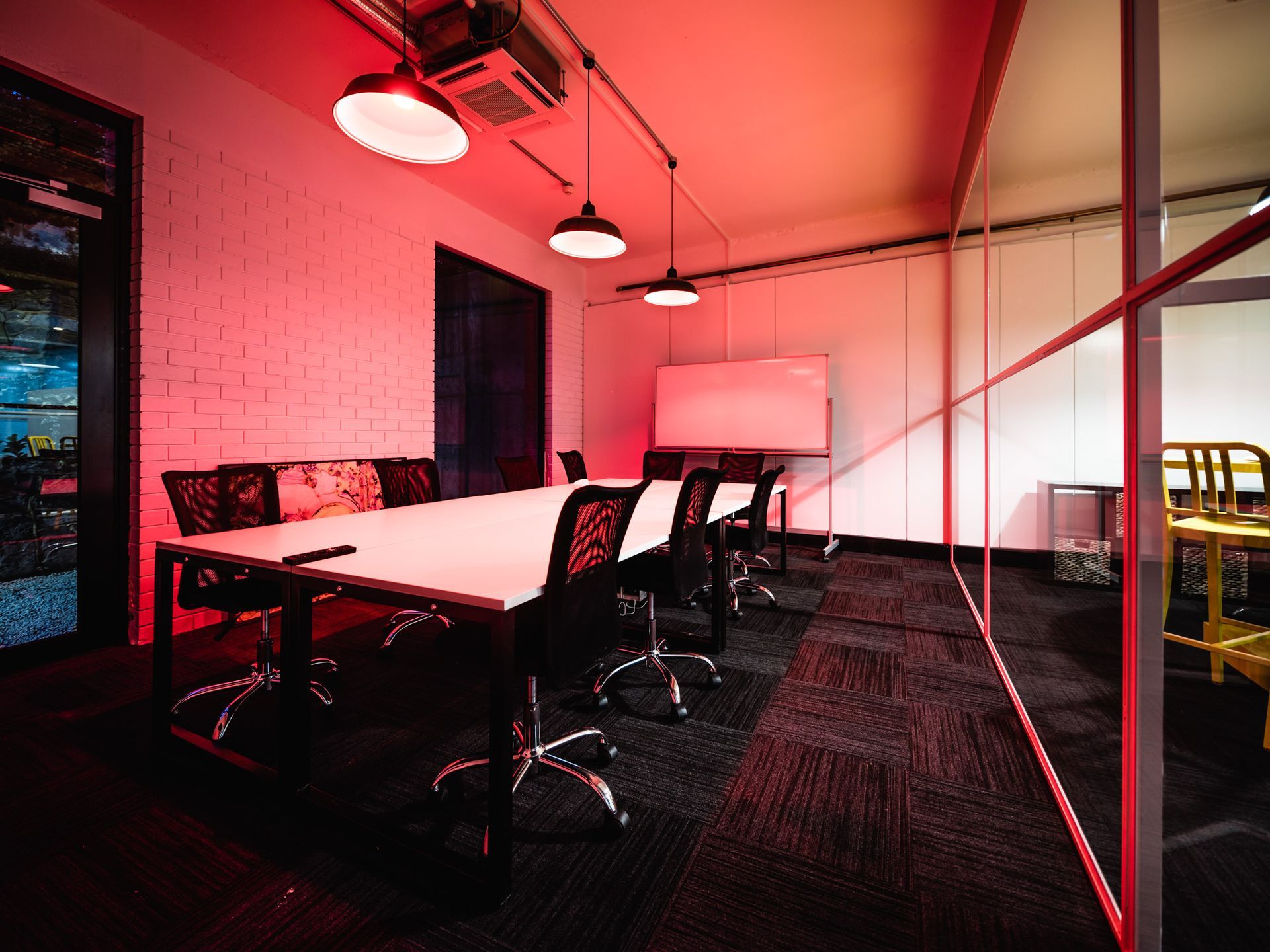 Modern conference room with a long table, black chairs, hanging lights, and a red-tinted glow