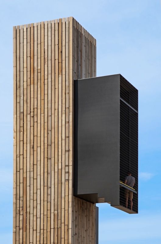 Modern building with vertical wooden slats and a dark cantilevered section against a blue sky