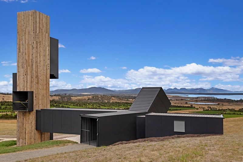 Modern black and wood building in a grassy landscape under a blue sky with mountains in the distance