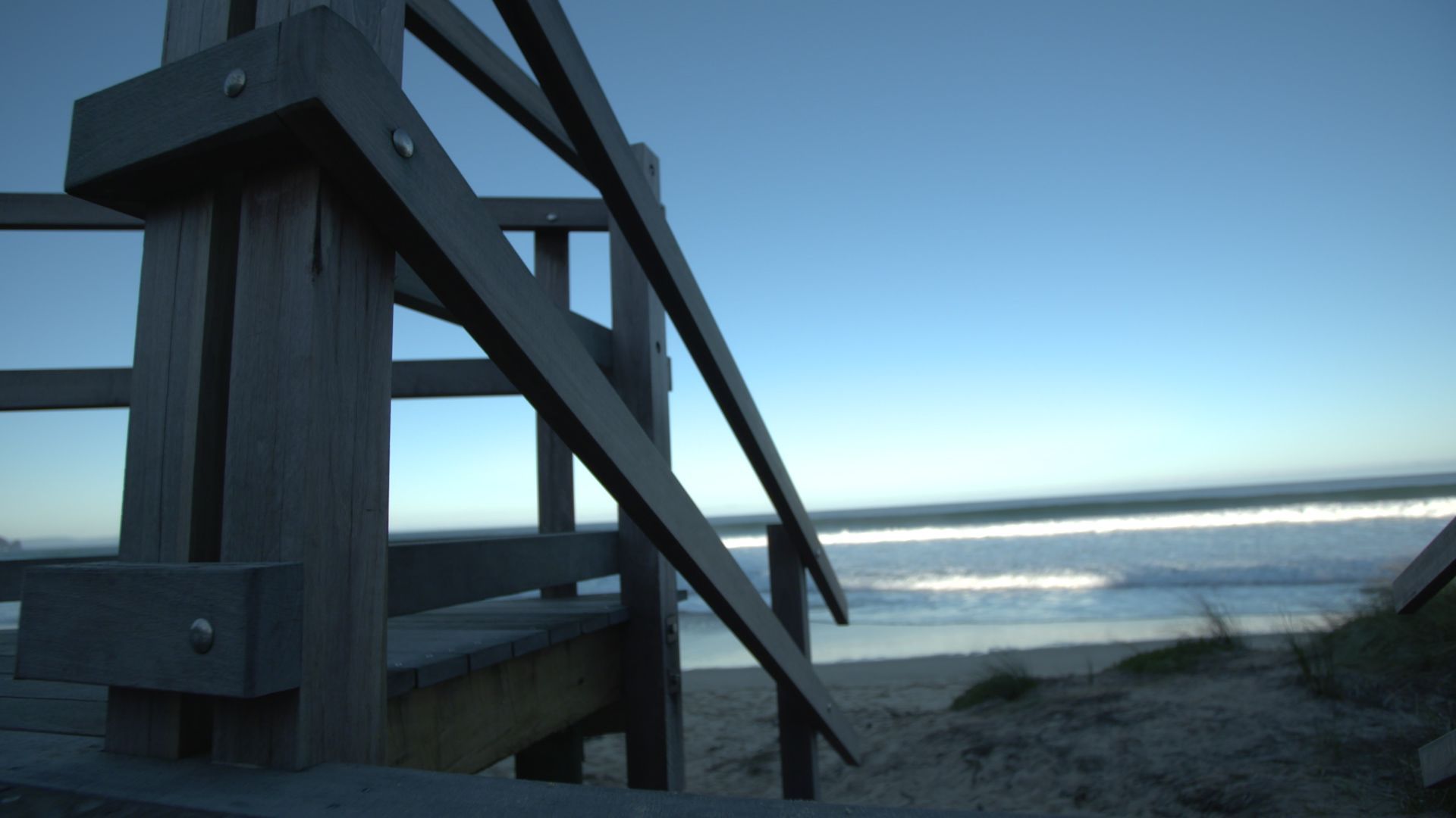 Wooden beach stairs overlooking a calm ocean at dawn or dusk.